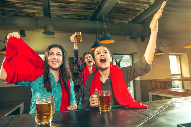 スポーツ、人々、レジャー、友情、エンターテインメントのコンセプト-幸せな女性のサッカーファンやビールを飲み、バーやパブでの勝利を祝う良い若い友人。人間のポジティブな感情の概念