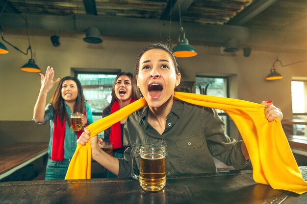 スポーツ、人々、レジャー、友情、エンターテインメントのコンセプト-幸せな女性のサッカーファンやビールを飲み、バーやパブでの勝利を祝う良い若い友人。人間のポジティブな感情の概念