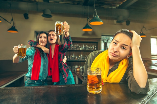 Sport, people, leisure, friendship, entertainment concept - happy female football fans or good young friends drinking beer, celebrating victory at bar or pub. Human positive emotions concept