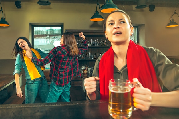 Sport, people, leisure, friendship, entertainment concept - happy female football fans or good young friends drinking beer, celebrating victory at bar or pub. Human positive emotions concept