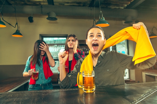 スポーツ、人々、レジャー、友情、エンターテインメントのコンセプト-幸せな女性のサッカーファンやビールを飲み、バーやパブでの勝利を祝う良い若い友人。人間のポジティブな感情の概念