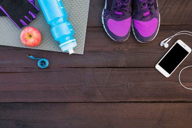 Sport shoes; cellphone; earphone; water bottle; glove; apple and measuring tape on wooden table