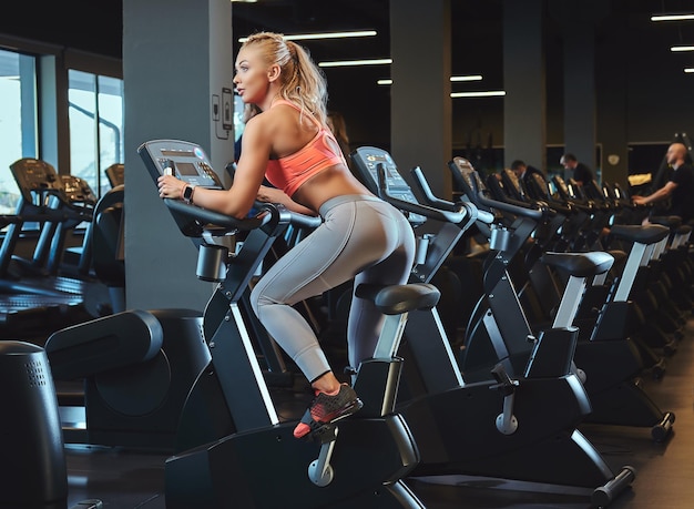 Sportive blonde woman working out on an exercise bike in a modern fitness center. Fitness lifestyle in sport club.