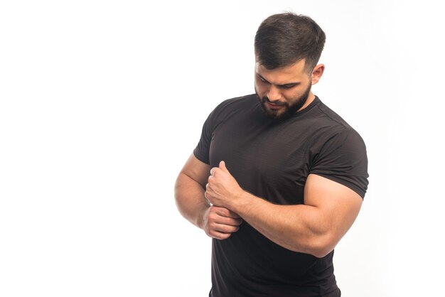 Sportive man in black shirt demonstrating his arm muscles. 