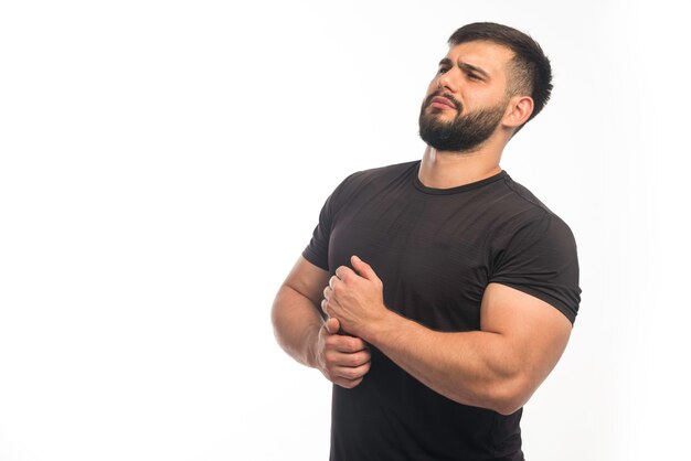 Sportive man in black shirt demonstrating his arm muscles. 