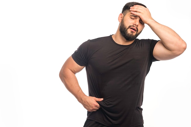 Sportive man in black shirt has a headache. 