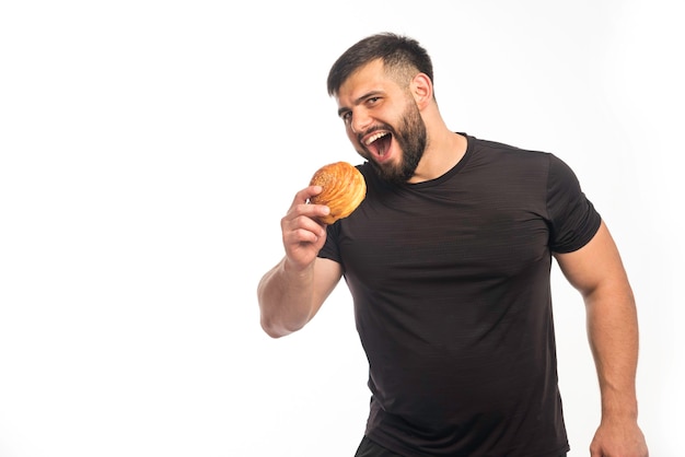 Uomo sportivo in camicia nera che tiene una ciambella e mangiare.