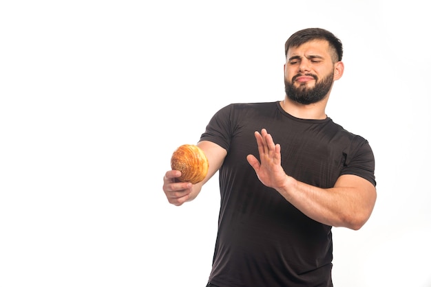 Sportive man in black shirt holding a doughnut and refusing. 