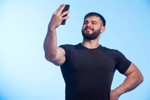 Sportive man in black shirt holds the phone and taking selfie