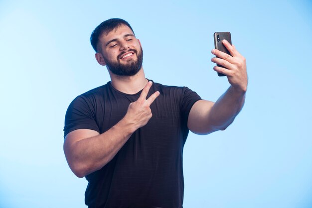 Sportive man in black shirt holds the phone and taking selfie. 