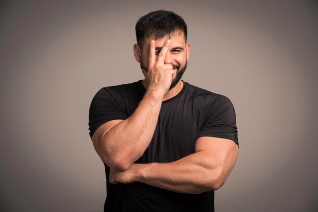 Sportive man in black shirt makes peace sign. 