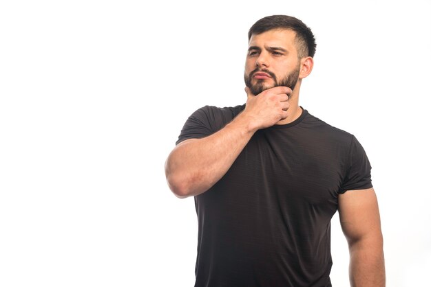 Sportive man in black shirt putting his hand to his beard. 