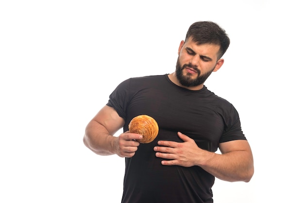 Спортивный мужчина в черной рубашке показывает пончик и держит живот