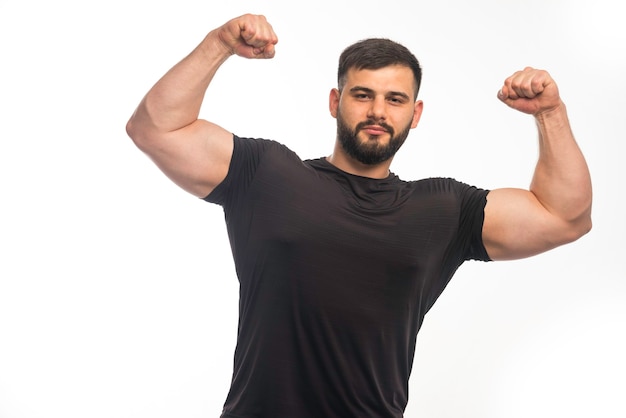 Спортивный мужчина в черной рубашке показывает мышцы руки.
