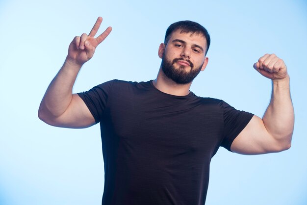 Sportive man in black shirt showing his muscles and making peace sign. 