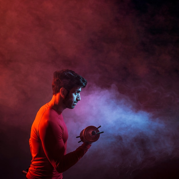 Sportive man lifting dumbbell in dark