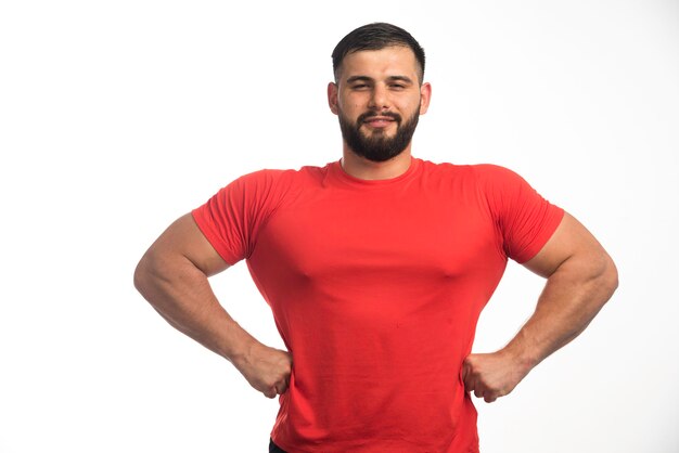 Спортивный мужчина в красной рубашке демонстрирует мышцы рук и выглядит уверенно.
