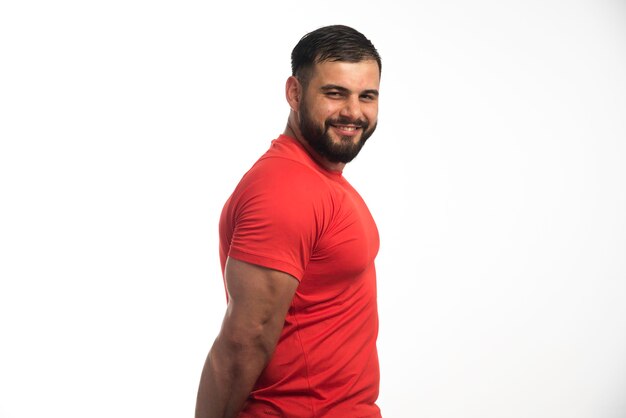 Free photo sportive man in red shirt demonstrating his arm muscles and smiling