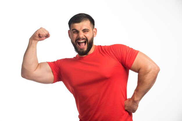 Sportive man in red shirt demonstrating his arm muscles and yelling. 