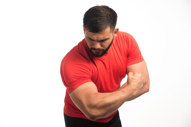 Sportive man in red shirt demonstrating his arm muscles . 