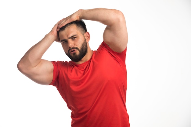 Foto gratuita uomo sportivo in camicia rossa che dimostra i suoi muscoli e ha messo le mani alla testa.