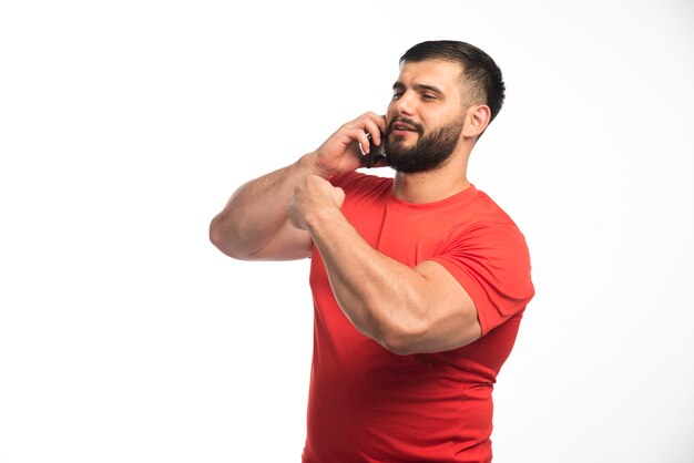전화로 얘기하고 그의 팔 근육을 보여주는 빨간 셔츠에 낚시를 좋아하는 남자.