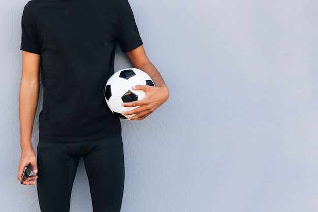 Foto gratuita uomo allegro che sta con il calcio e telefono