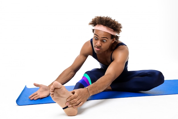 Sportive man stretching, sitting on yoga mat