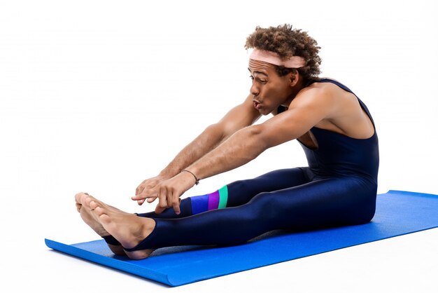 Спортивный человек растягивается, сидя на коврике для йоги