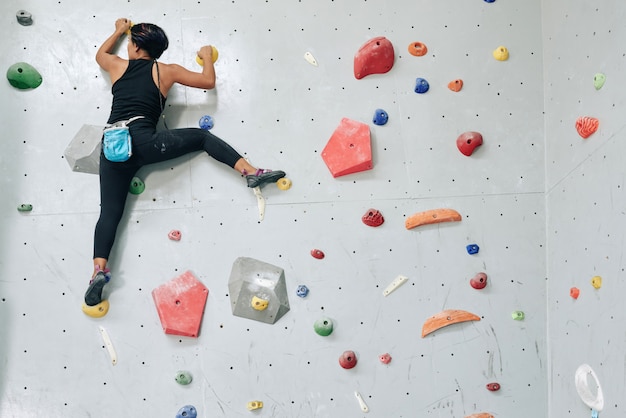 Sportive woman clambering wall in gym