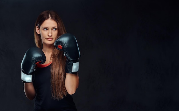 Donna sportiva vestita di abbigliamento sportivo che indossa guanti da boxe in posa in uno studio. isolato su sfondo scuro con texture.