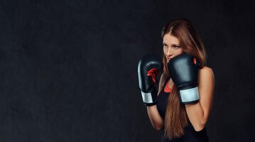 Sportive woman dressed in sportswear wearing boxing gloves posing in a studio. isolated on dark textured background.