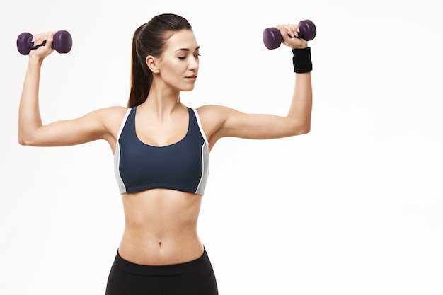 Sportive woman in sportswear training arms with dumbbells on white.