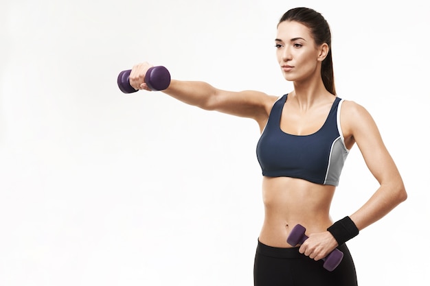 Sportive woman in sportswear training arms with dumbbells on white.