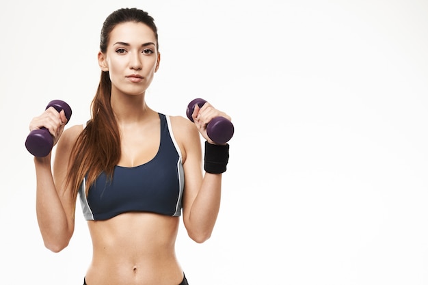 Sportive woman with dumbbells in sportswear posing on white.