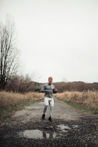 Foto gratuita giovane atleta maschio allegro che funziona sulla strada non asfaltata