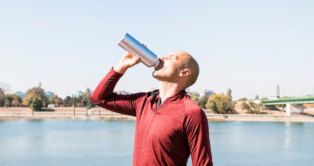 陽気な若い男、湖の近くに立っているボトルから水を飲む