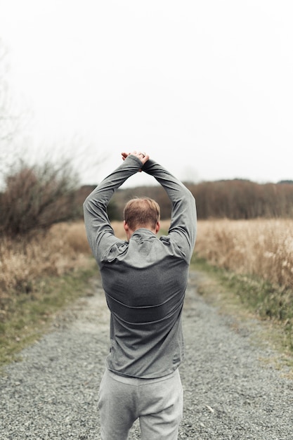 Sportive young man stretching his hand on countryside road