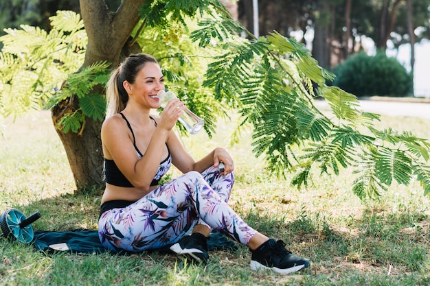 Спортивная молодая женщина, наслаждаясь питьевой водой из бутылки в саду