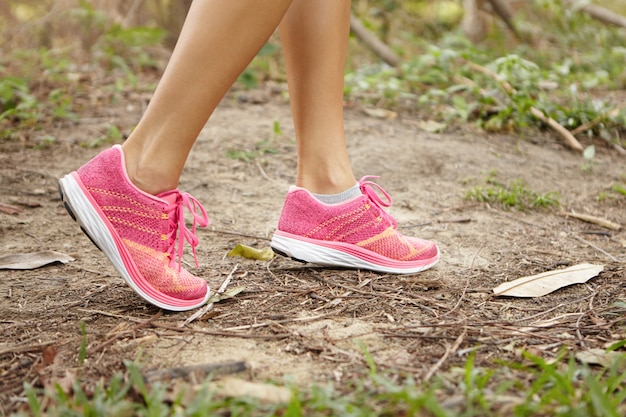 Sports and adventure concept. Close up shot of female legs wearing pink running shoes in forest while exercising in summer nature.