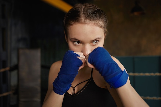 Sports, fighting, training and physical exercise concept. Indoor shot of concentrated young Caucasian woman wearing top and handwraps clenching fists