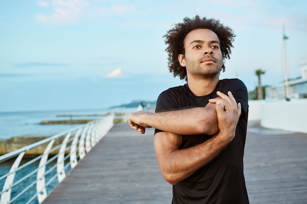 Sports, fitness and healthy lifestyle. Fit young Afro-American man doing warm-up before running on the boardwalk in the morning.