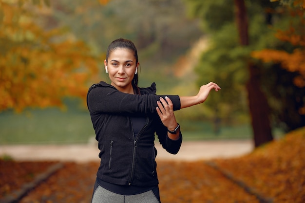 Спортивная девушка в чёрном топе тренируется в осеннем парке