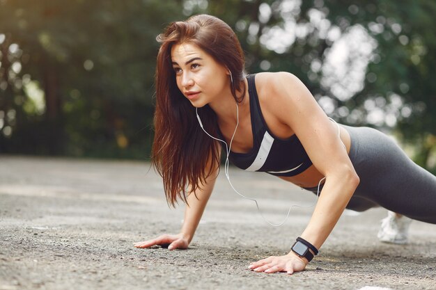 Sports girl training with headphones in a summer park