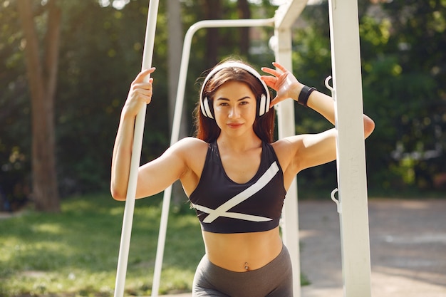 Sports girl training with headphones in a summer park