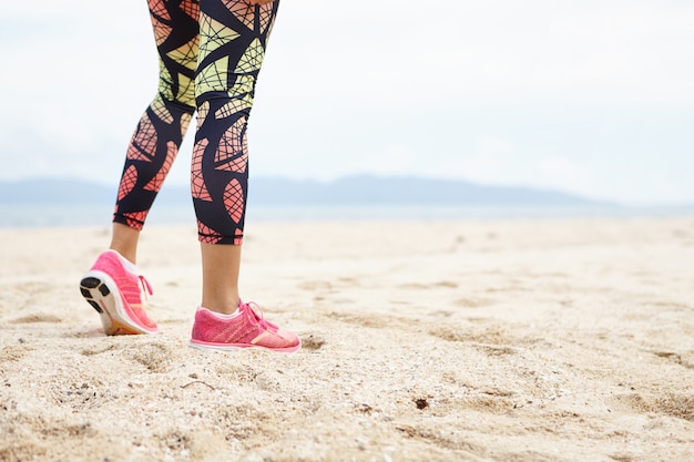 Sports and healthy lifestyle concept. Cropped shot of legs of girl athlete against ocean beach.