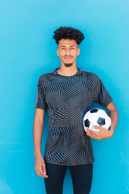 Free photo sportsman holding soccer ball under arm near wall