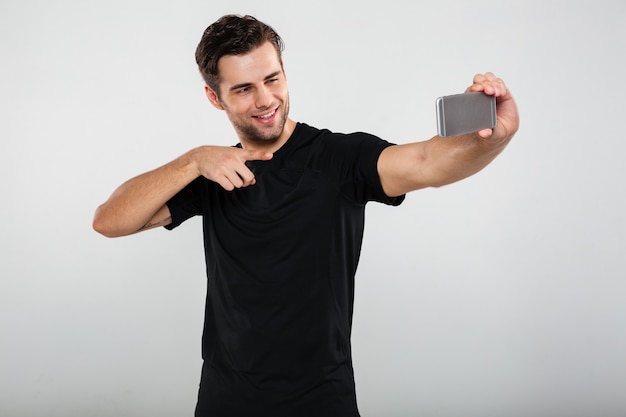 Lo sportivo fa selfie indicando il telefono cellulare.