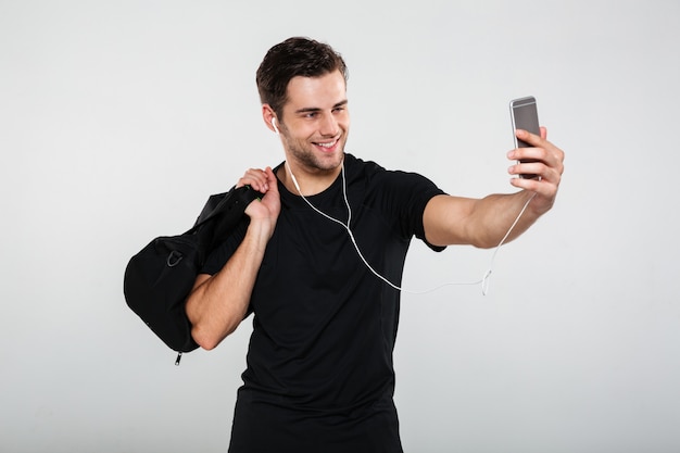 スポーツマンは音楽を聴く携帯電話でバッグとselfieを作る