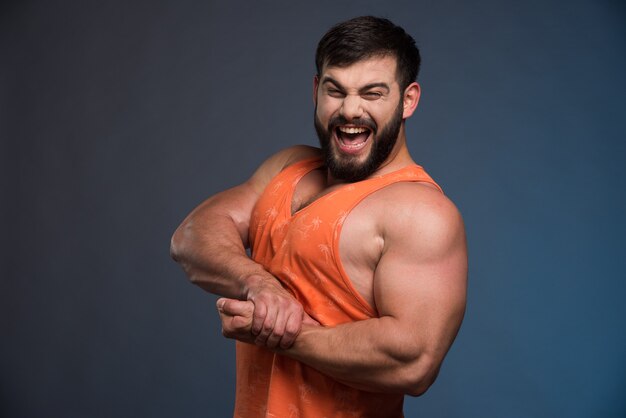 Sportsman showing his muscles on dark blue wall.